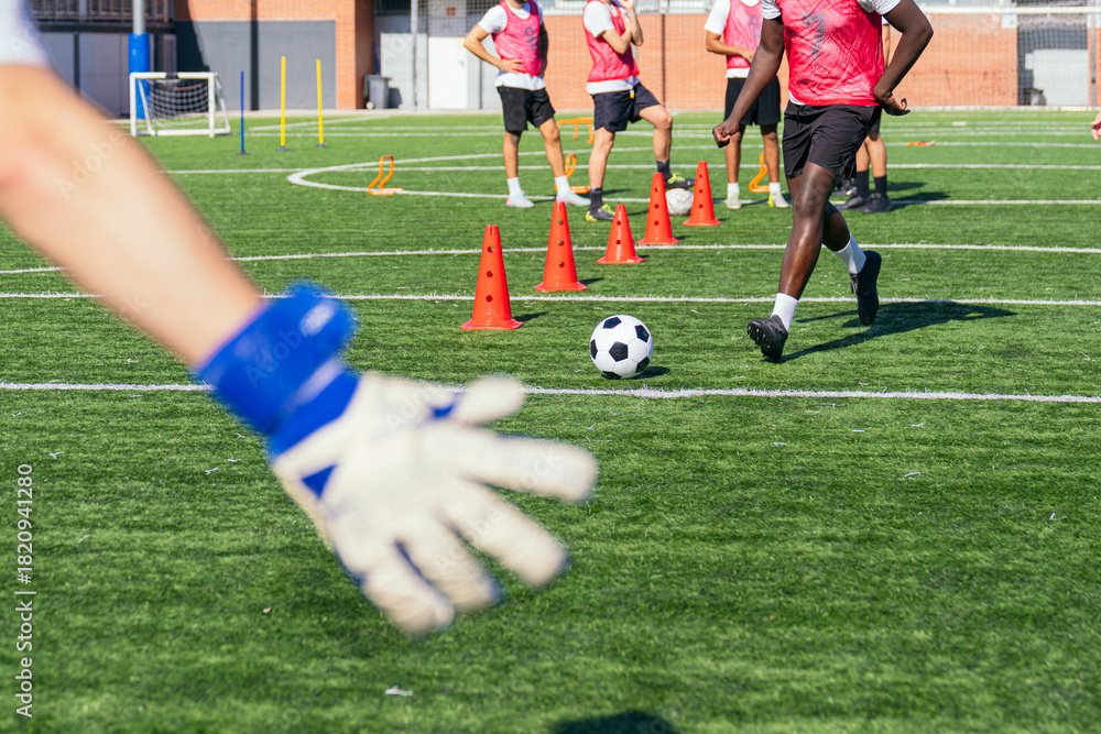 Naklejka premium Goalkeeper's outstretched hand reaching towards a soccer ball during intensive football practice with team players