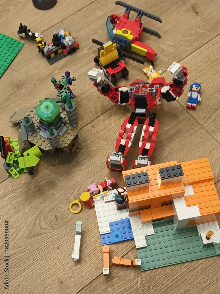 Naklejka premium A collection of colorful LEGO creations, including a Marvel superhero mech and a Minecraft-style building, scattered on a wooden floor during playtime