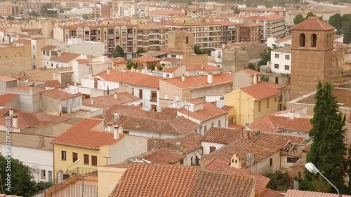 Urban view of Guadix with a historic church tower standing out among red rooftops and residential buildings. A typical Andalusian village landscape that blends the old and the new in Spain.