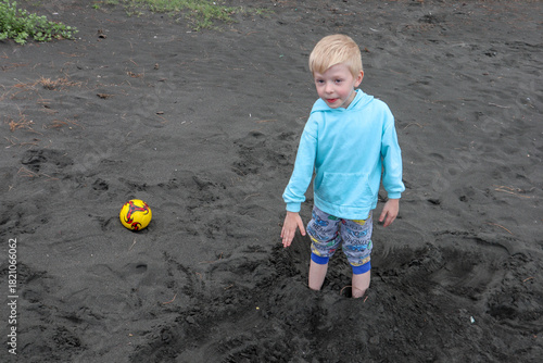 Little blond kid play football and have fun on black sand beach in Kobuleti, Georgia