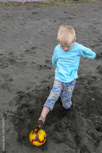 Little blond kid play football and have fun on black sand beach in Kobuleti, Georgia