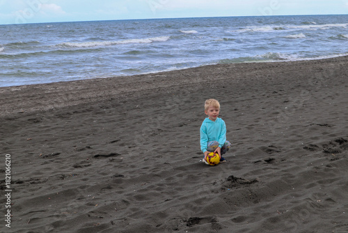 Little blond kid play football and have fun on black sand beach in Kobuleti, Georgia