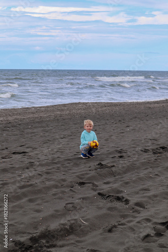 Little blond kid play football and have fun on black sand beach in Kobuleti, Georgia