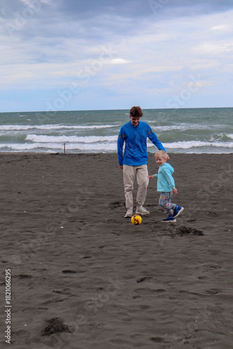 Two brothers play football and have fun on black sand beach in Kobuleti, Georgia