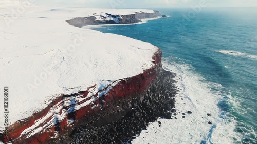 Wallpaper Mural Aerial view of storm ocean waves crashing against snowy coastal cliffs at winter sunrise. The Icelandic plateau reveals striking, martial red mineral cliffs contrasted against the icy landscape Torontodigital.ca