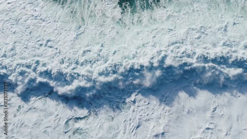 Aerial view from a drone flying through a winter snowstorm as a powerful ocean wave crashes over snow-covered volcanic cliffs. Stormy winter surf batters the rugged Icelandic coast