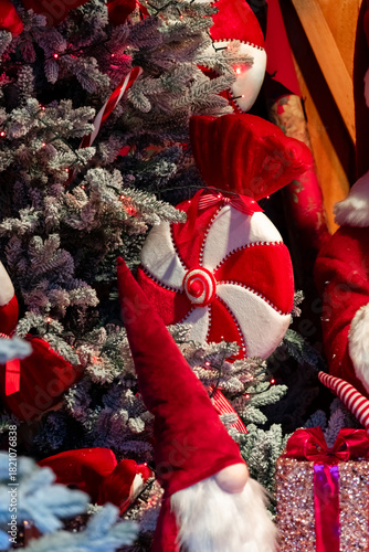 Close-up of a decorated Christmas tree with a large red-and-white peppermint ornament, festive ribbons, and warm holiday lights