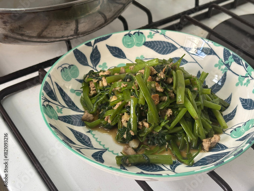 A vibrant dish of stir-fried morning glory, featuring tender greens and minced meat in a glossy oyster sauce. Served in a decorative bowl, this appetizing meal showcases fresh ingredients.