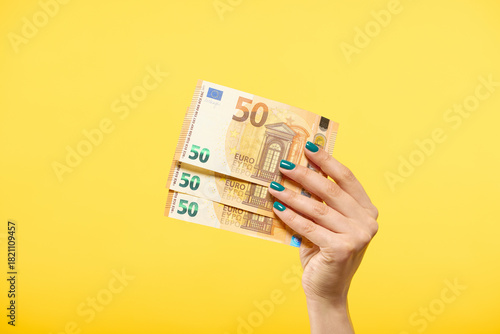 Woman hand holding euros banknotes isolated on yellow background. Finance concept.