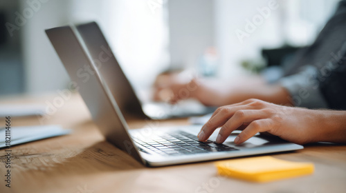Close-up of hands typing on laptop keyboard in modern environment with blurred background and wooden desk