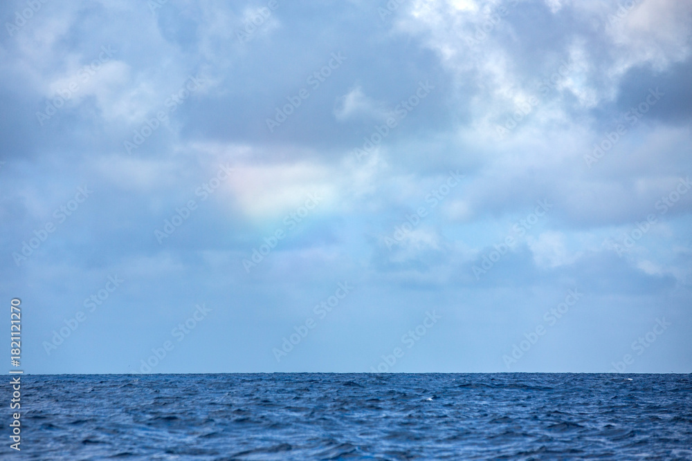 Fototapeta premium An idyllic tropical blue ocean featuring a feint rainbow in the storm clouds above the horizon.