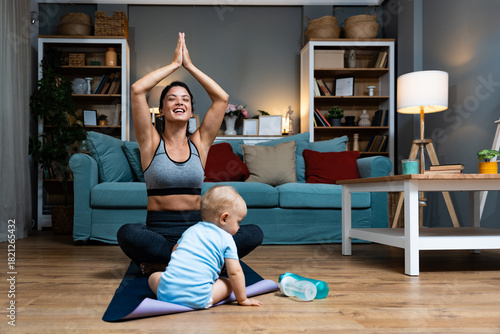Young mother practicing yoga at home with baby nearby balancing postpartum recovery mindfulness gentle movement during evening workout joy family bonding on mat calm wellness routine for active parent