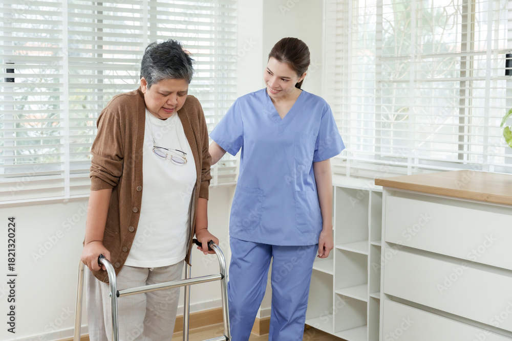 Obraz premium Young asian female physiotherapist encouraging senior asian woman walking with walker at home focusing on physical therapy progress and mobility support for elderly care rehabilitation