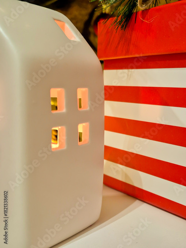 A white ceramic house with a candle inside and a Christmas gift box.