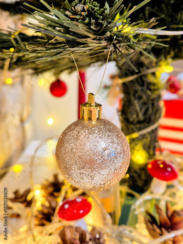 A gold bauble on the Christmas tree. Festive decorations and a glowing garland with warm light.