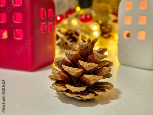 A pinecone and Christmas decorations in the background. Ceramic houses, candles, and a glowing garland.
