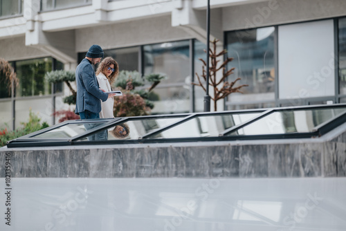 Wallpaper Mural Two colleagues and friends discuss ideas outdoors by a modern glass skylight in a city setting, sharing a notebook and planning a project with calm, collaborative energy. Torontodigital.ca