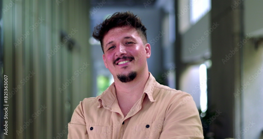 Obraz premium Close-up of smiling man with short hair and facial hair in modern office hallway, arms crossed and exuding confidence and warmth
