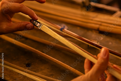 Violin making by hand bow. Close-up of an artisan’s hands sanding or shaping a tool handle on a workbench. 