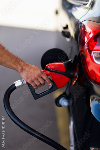 Close-up of a person’s hand holding a fuel pump nozzle while refueling a car at a gas station. The image shows transportation, energy, and daily vehicle usage.