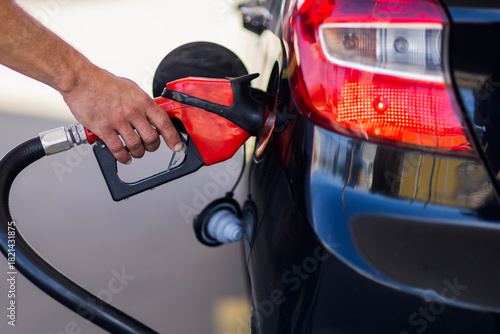 Close-up of a person’s hand holding a fuel pump nozzle while refueling a car at a gas station. The image shows transportation, energy, and daily vehicle usage.