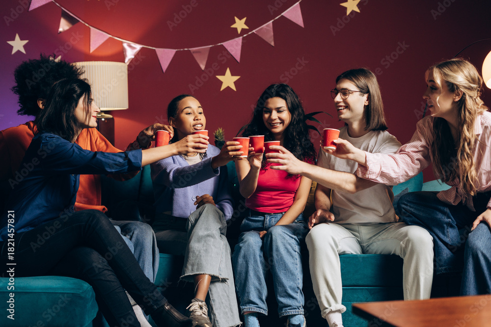 Fototapeta premium Diverse young friends celebrating and toasting with red cups at a fun house party