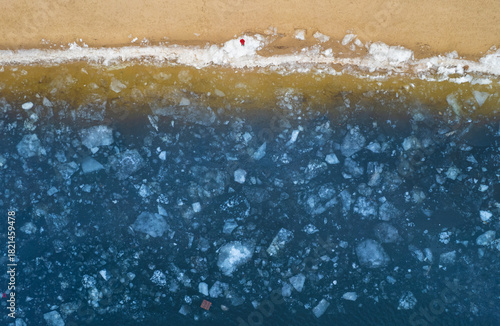 Aerial top down view of a frozen river bank with broken ice.