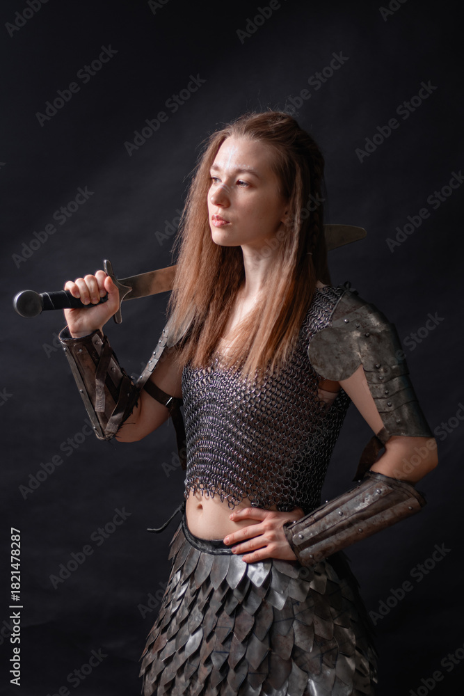 Obraz premium Portrait of a young woman, fantasy warrior in armor with a sword in her hands isolated on a dark background.