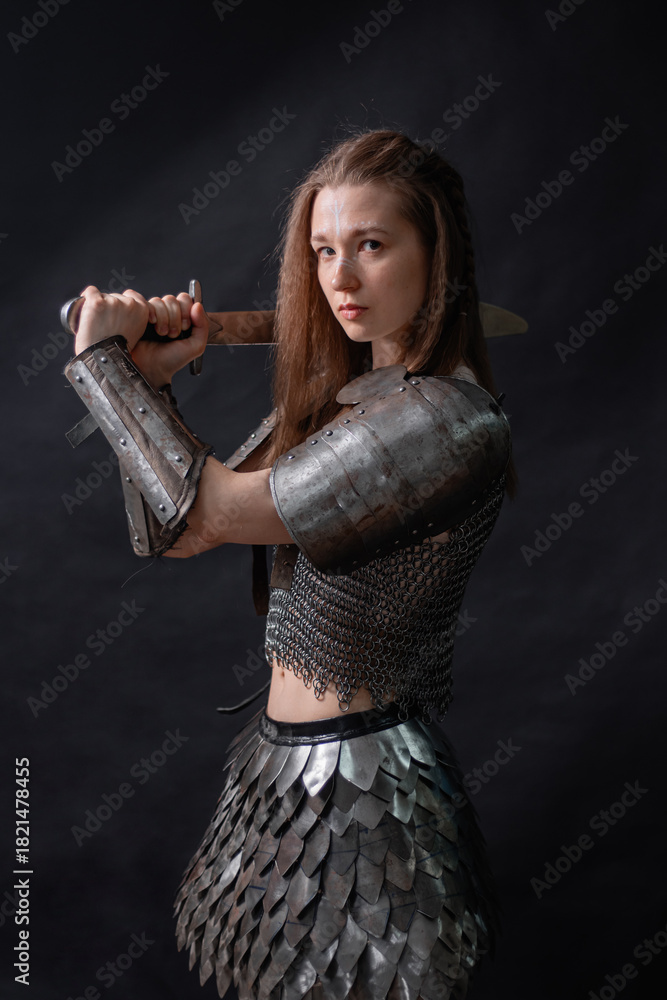 Naklejka premium Portrait of a young woman, fantasy warrior in armor with a sword in her hands isolated on a dark background.