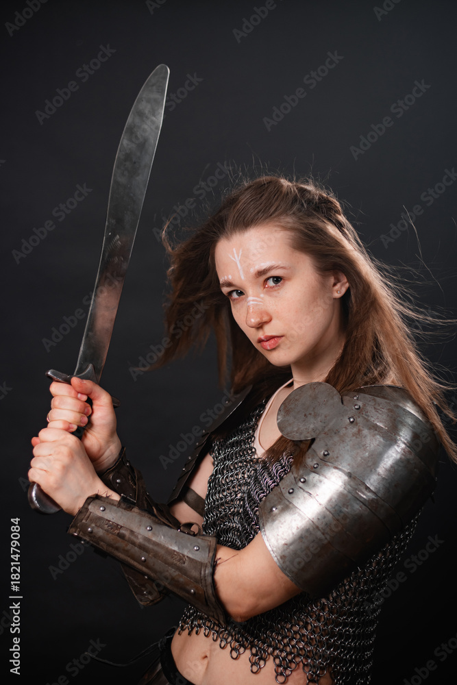 Fototapeta premium Portrait of a young woman, fantasy warrior in armor with a sword in her hands isolated on a dark background.
