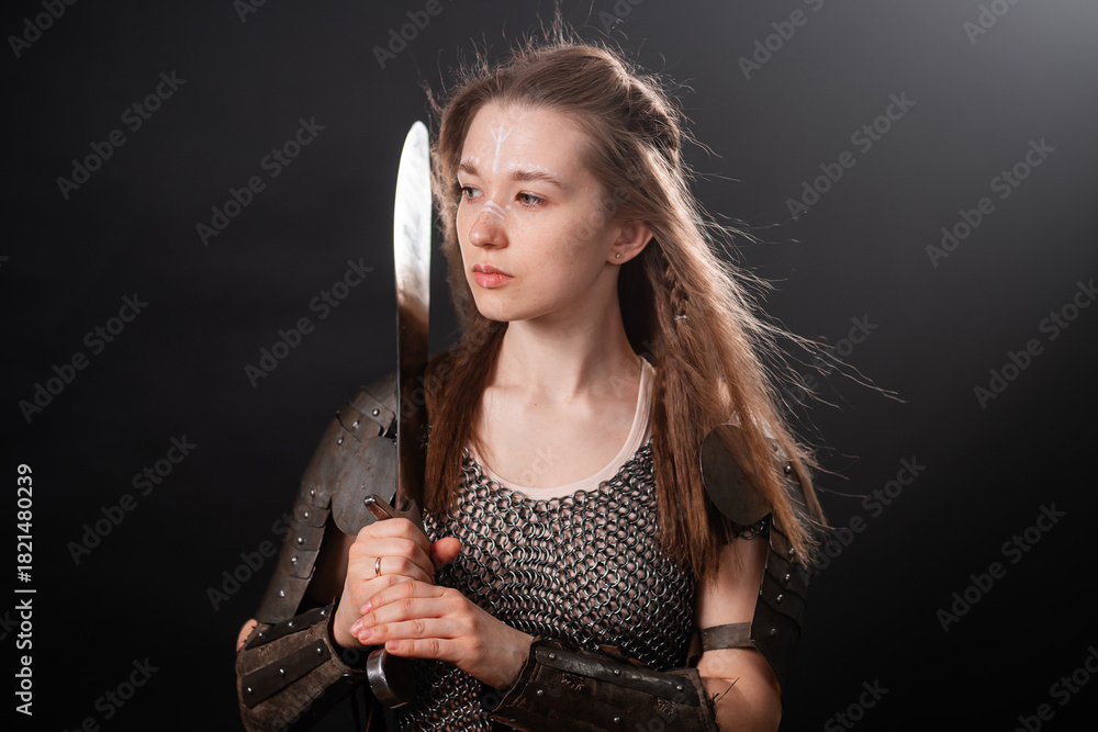 Fototapeta premium Portrait of a young woman, fantasy warrior in armor with a sword in her hands isolated on a dark background.