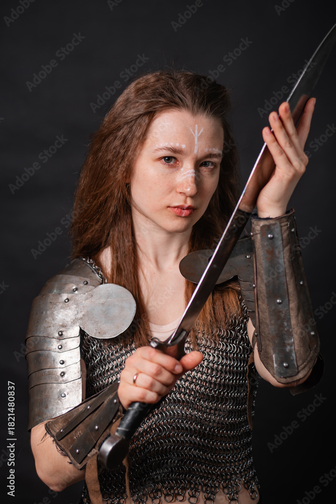 Naklejka premium Portrait of a young woman, fantasy warrior in armor with a sword in her hands isolated on a dark background.