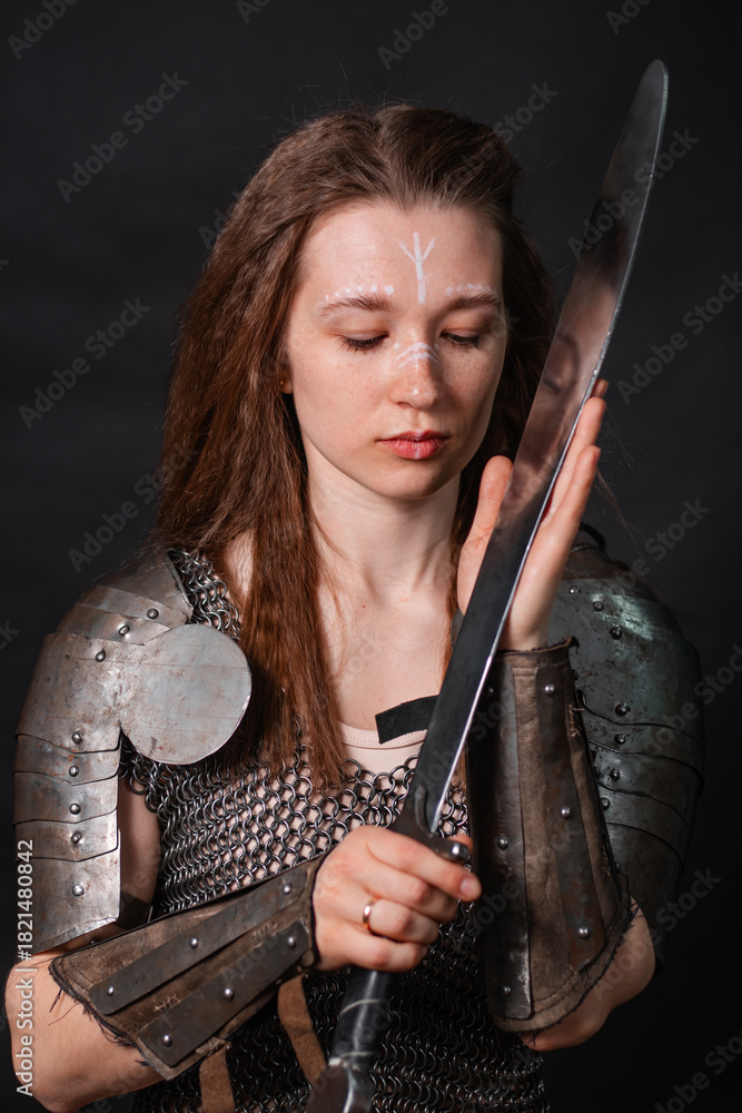 Naklejka premium Portrait of a young woman, fantasy warrior in armor with a sword in her hands isolated on a dark background.