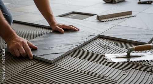 Laying tile flooring: Hands arrange tiles in a linear pattern, accompanied by trowel and grout float tools. Visually appealing and organized appearance.