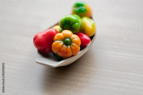 Colorful Thai mung bean desserts (look choop) shaped like mini fruits and vegetables, displayed beautifully in a small ceramic plate on a wooden table. Traditional Thai sweet.