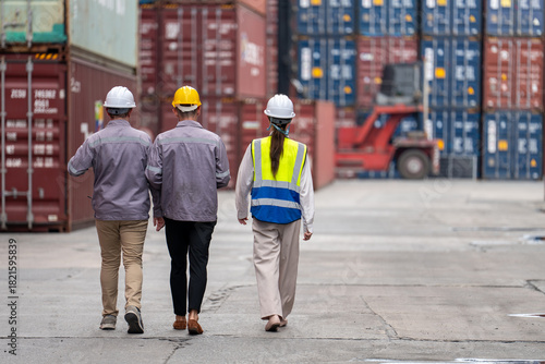 Team logistics professionals in safety gear discussing and inspecting stacked cargo containers, planning operations at shipping yard.