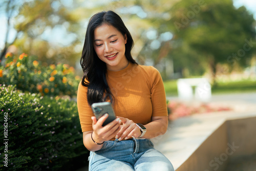 Asian woman smiling using smartphone outdoors in park
