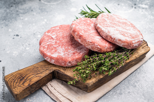 Frozen raw Hamburger beef Patty, uncooked mincemeat. grey background. top view