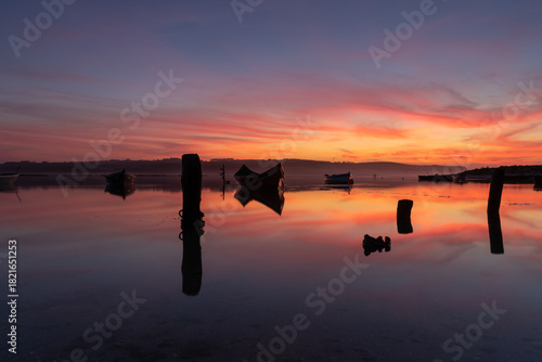 Photography Sunset reflected in a mirror-like body of water with silhouettes of boats and other elements in an atmosphere of peace and tranquility