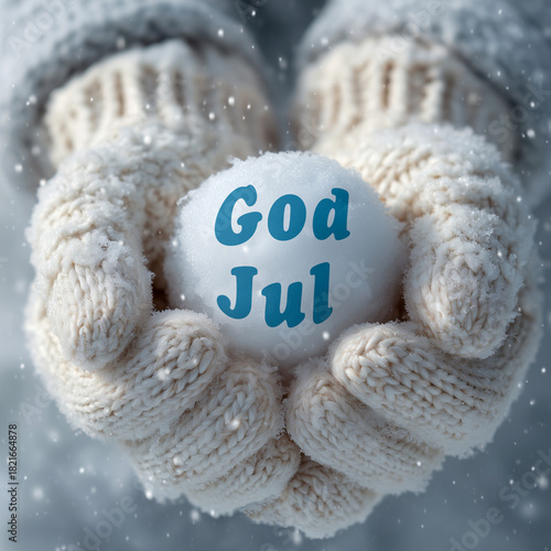 God Jul. Merry Christmas. View of cozy white knitted mittens (gauntlets) holding a perfectly round snowball, palms facing the viewer, soft winter lighting. Falling snow. Scandinavian greeting.