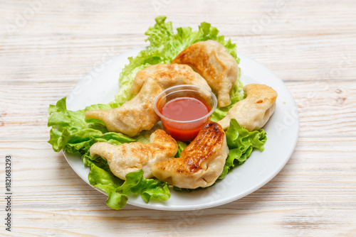 Raviolis grillés sur assiette blanche avec feuille de salade et sauce piquante. Cuisine chinoise. Traiteur chinois.