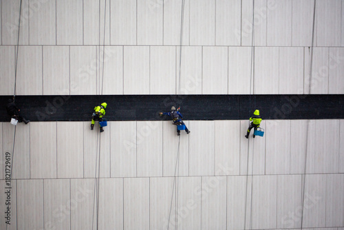 Large group of industrial climbers work at height and clean the building facade. Team specializing in working at height. Worker safety and insurance. Industrial climbing concept