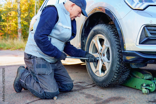 Precision on the ground — mechanic kneels by a raised car, firmly adjusting bolts on the wheel with full-body focus and roadside light.