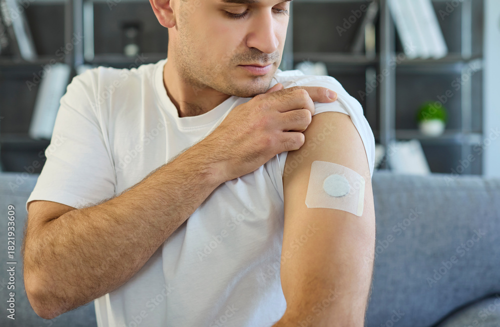 Obraz premium Man shows arm patch for diabetes sensor. The glucose monitor is a wearable medical device for health tracking at home, secured with adhesive on the arm. Concept: wearable diabetes care device.
