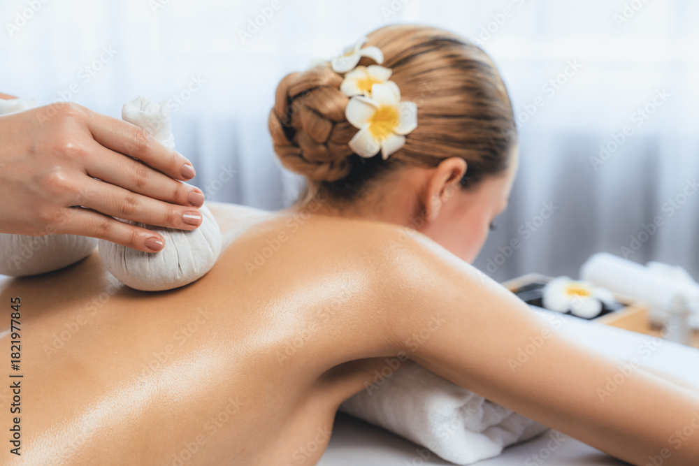 Obraz premium Hot herbal ball spa massage body treatment, masseur gently compresses herb bag on woman body. Tranquil and serenity of aromatherapy recreation in day lighting ambient at spa salon. Quiescent