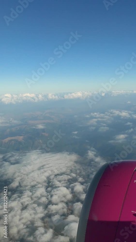 Vertical 4K view from an airplane cabin showing the engine, clouds, and mountains below during a calm flight