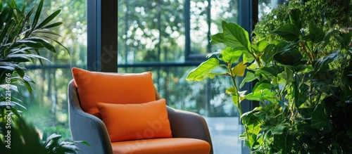 Fototapeta Naklejka Na Ścianę i Meble -  Modern armchair with orange cushions by a bright window, surrounded by green plants, creating a comfortable and natural interior living space.