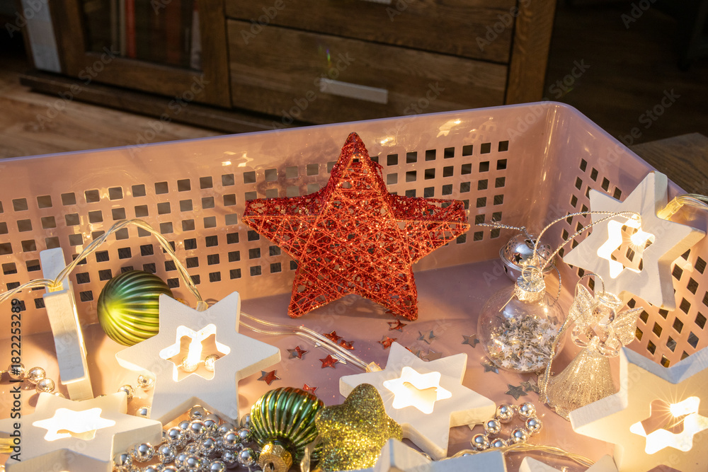 Fototapeta premium Holiday decoration: red wire stars and New Years garland in the form of six-pointed stars in a pink storage basket. Christmas decor, seasonal storage, holiday preparation. Real photo