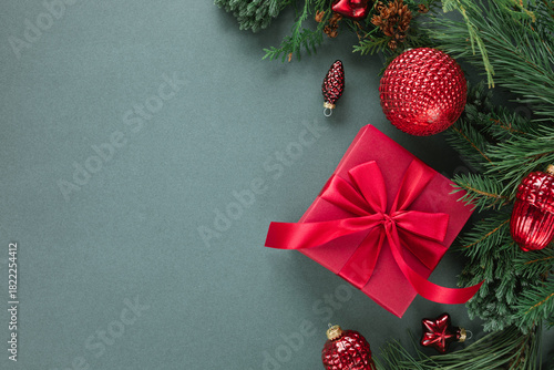 Overhead view of a wrapped Christmas gift box, festive Christmas baubles and ornaments with fir branches on a green background