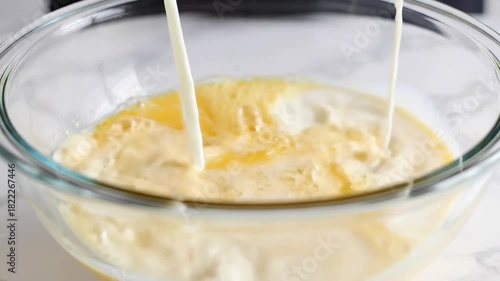 Milk pouring into a bowl of yellow batter cooking process.